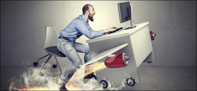 A man using a desktop computer with jet engines strapped to his desk.