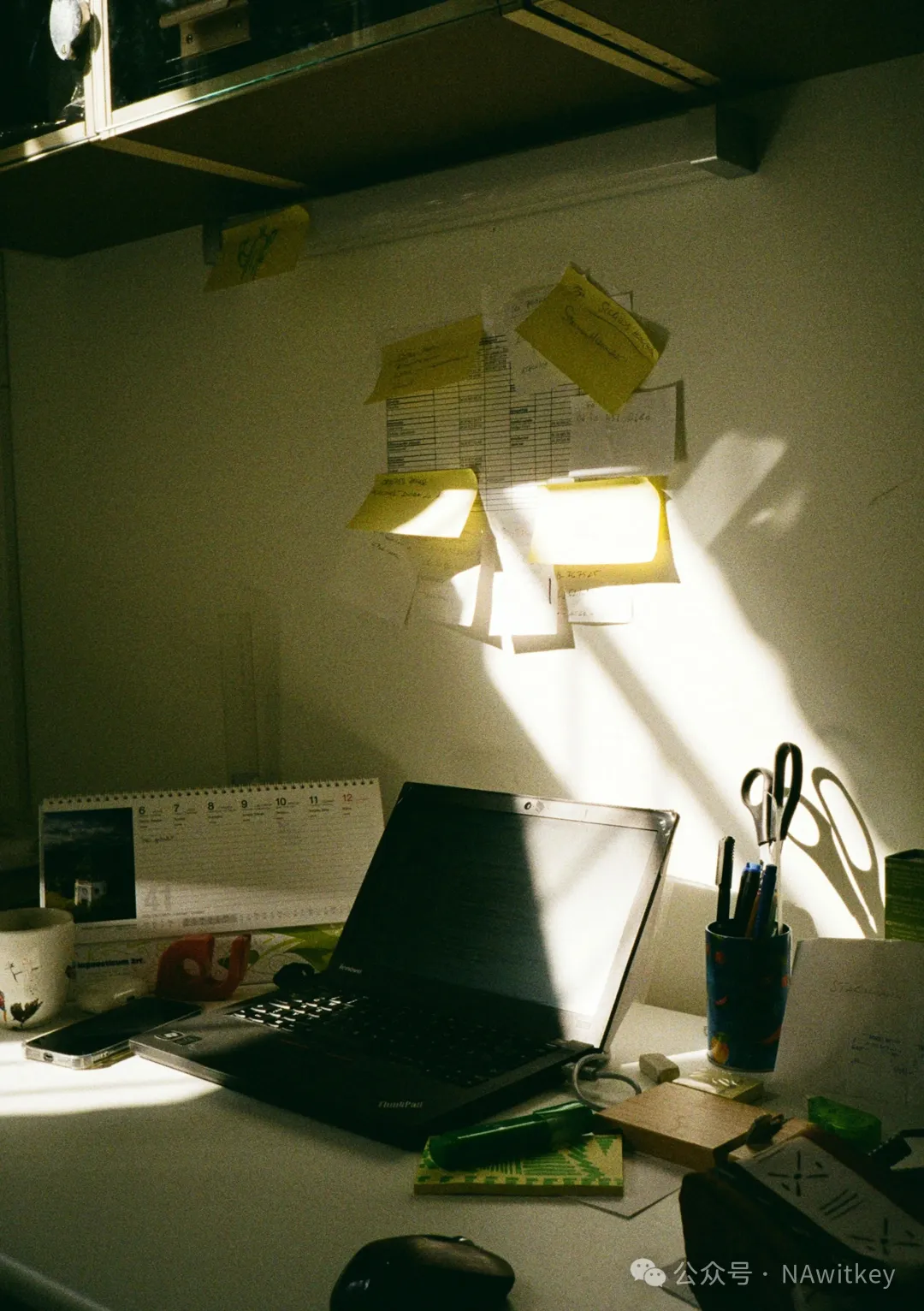 Desk with laptop, sticky notes, and sunlight.